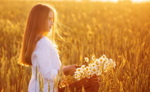 Flicka i fältet vete med korg med blommor — Stockfoto