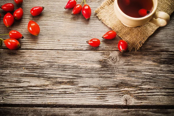 Tasse Tee mit Hüftrosen, auf Holztisch — Stockfoto