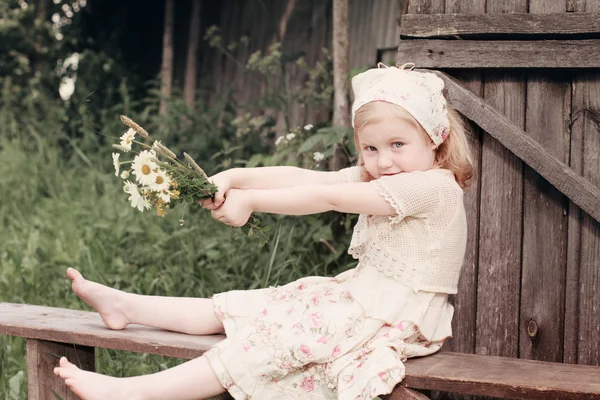 Little girl with flowers on wooden bench — Stock Photo, Image