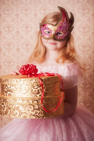 Liten flicka i festlig klänning med present och carnival mask — Stockfoto