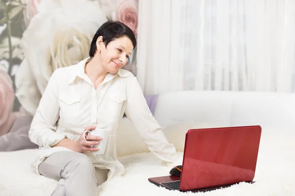 Nő használ laptop, miközben otthon ül az ágyon — Stock Fotó
