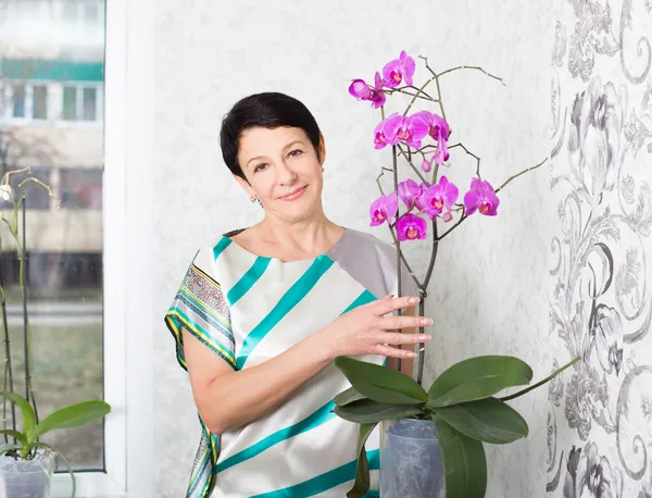 Happy mature woman with Phalaenopsis orchid indoor — Stock Photo, Image