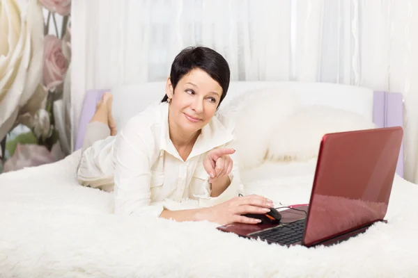 Женщина с ноутбуком, сидя дома на кровати — стоковое фото