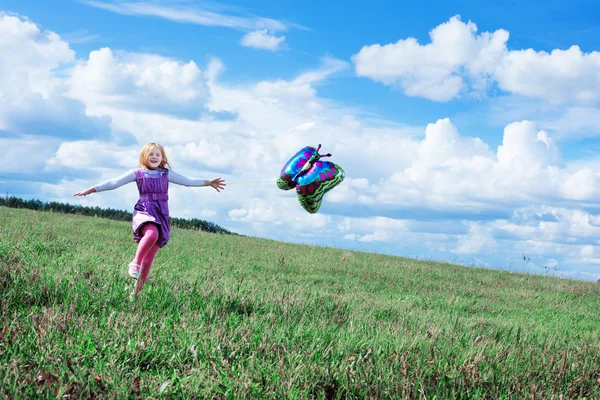 Маленькая девочка играет с воздушным шаром в траве — стоковое фото