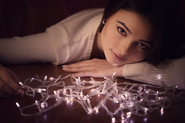 Beautiful woman sitting at table with Christmas light garland — Stock Photo, Image