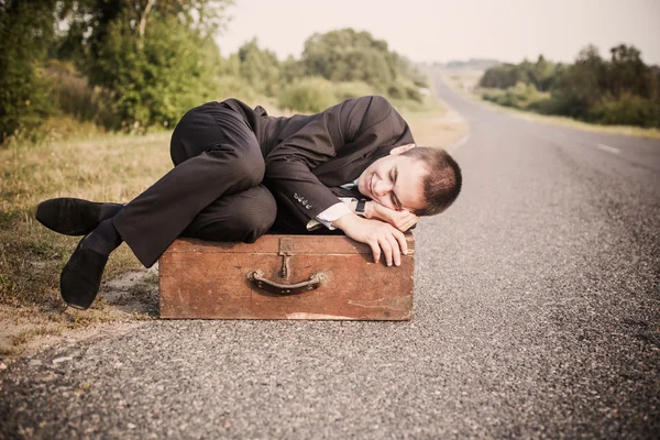 Jeune homme repose sur la vieille valise sur la route — Photo