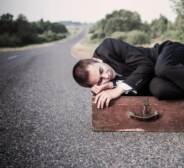 Jeune homme repose sur la vieille valise sur la route — Photo