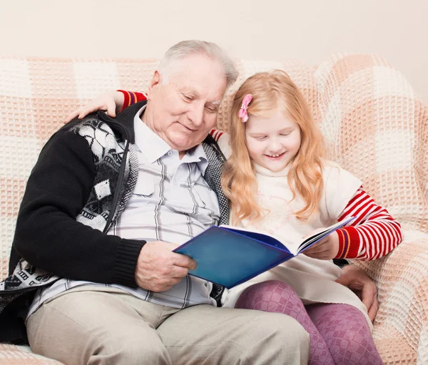 Grandfather and granddaughter sitting on the sofa and reading bo — Stock Photo, Image