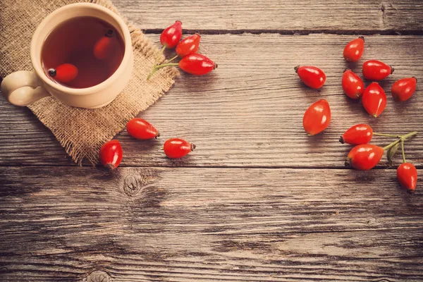 Cup of tea with hip roses, on wooden table — Stock Photo, Image