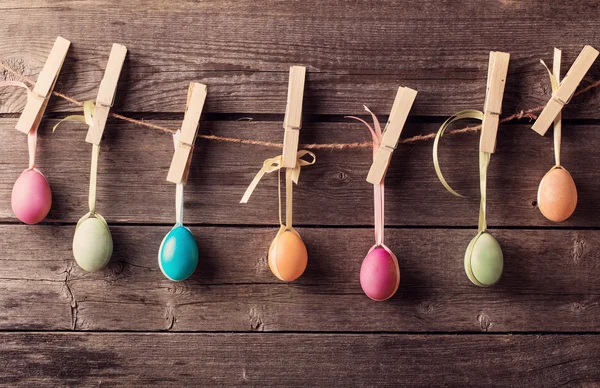 Huevos de Pascua se unen a la cuerda con alfileres de ropa en el fondo de madera — Foto de Stock