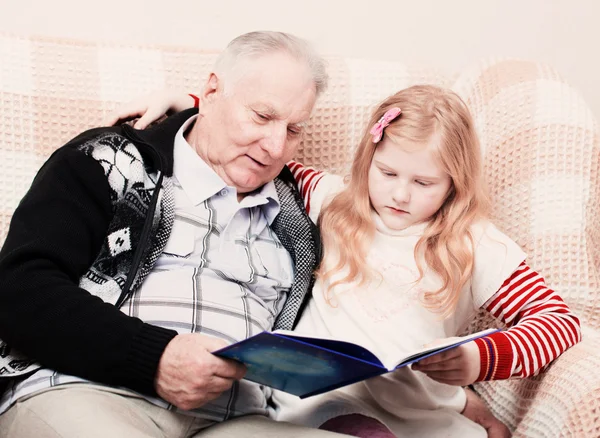 Grandfather and granddaughter sitting on the sofa and reading bo — Stock Photo, Image