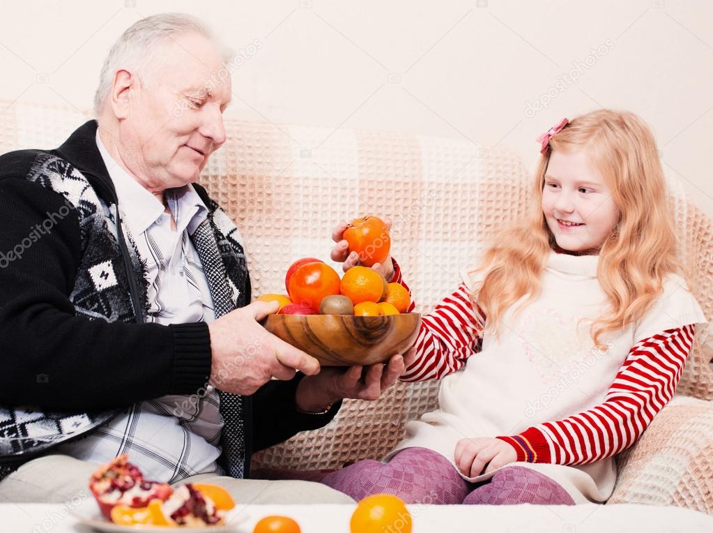 Grandfather with smile girl eating fruits at home