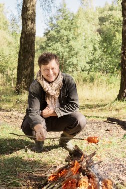 kamp ateşi oturan olgun bir gülümseme adam