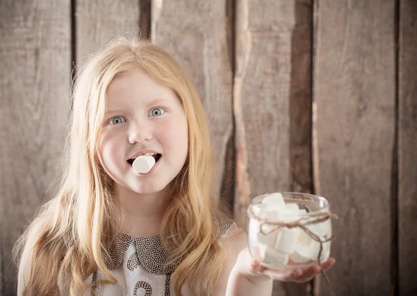 Meisje met marshmallows op houten achtergrond — Stockfoto