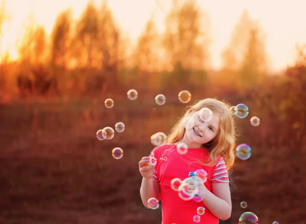 Girl blowing soap bubbles outdoor at sunset — Stock Photo, Image