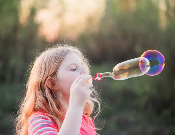 Menina soprando bolhas de sabão ao ar livre ao pôr do sol — Fotografia de Stock