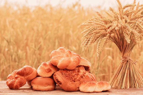Pane e grano sul tavolo di legno nel campo autunnale — Foto Stock