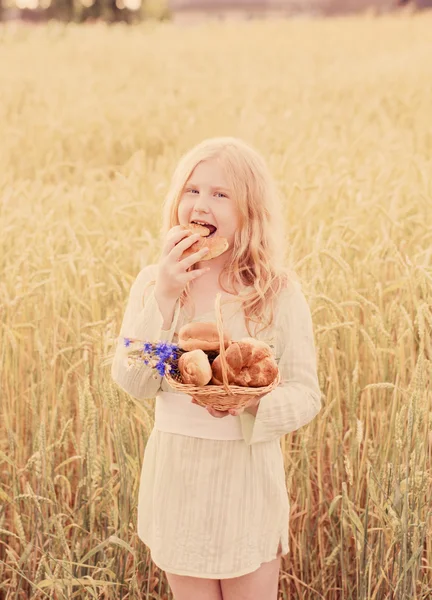 Carino bambina mangiare pane sul campo di grano — Foto Stock