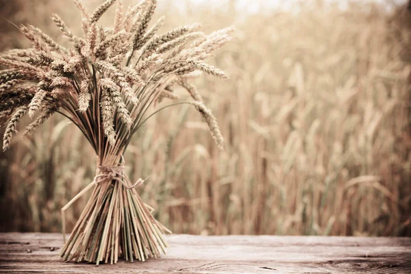 Eerstelingsgarve op houten tafel op achtergrond veld — Stockfoto