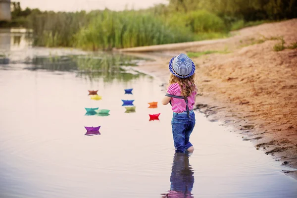 Ребенок играет с бумажными лодками в реке — стоковое фото