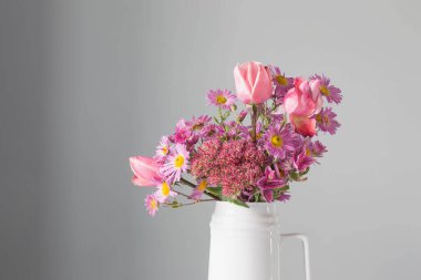 Arka planda beyaz sürahide pembe çiçekler gri duvarda