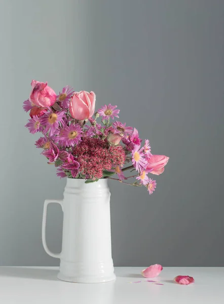 背景の灰色の壁に白いジャグのピンクの花 — ストック写真