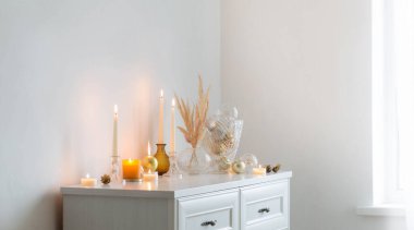 Beyaz odada yanan mumlarla Noel süsleri.