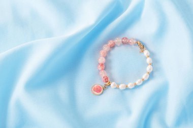 Pembe ve beyaz bilezik mavi ipek kumaşta doğal taşlardan yapılmıştır.