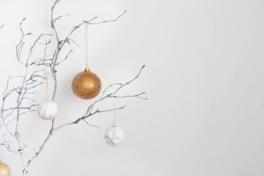 Beyaz duvar arkasında altın ve beyaz topları olan Noel dalları