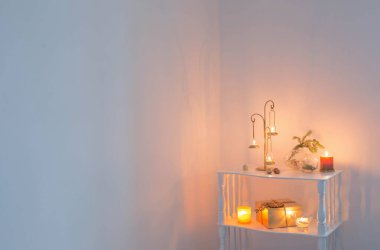 Altın şamdan, yanan mumlar ve ahşap raflarda noel süsleri.