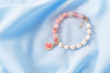 Pembe ve beyaz bilezik mavi ipek kumaşta doğal taşlardan yapılmıştır.