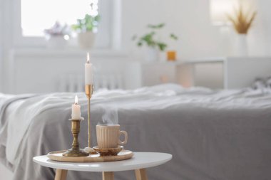 Beyaz yatak odasında mumlu bir fincan kahve.