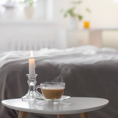 Yatak odasında yanan mum olan bir fincan kahve.