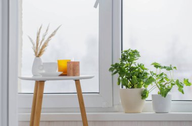 Kışın pencerenin yanındaki beyaz masada yanan mumlarla bir fincan kahve.