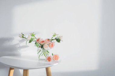 Pembe güller cam kavanozda beyaz masa üzerinde beyaz arka plan beyaz duvarda