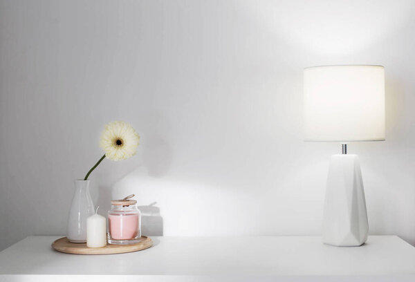 gerber in vase, candles and modern lamp on white shelf