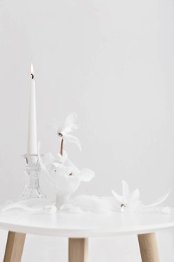 Kırık cam vazo, beyaz siklamen ve yanan mum.