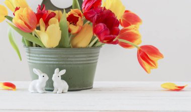 Kovada kırmızı ve sarı laleler ve beyaz arka planda seramik tavşan.