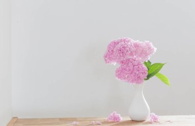 Beyaz vazodaki pembe ortanca arka plandaki ahşap rafta beyaz duvarda