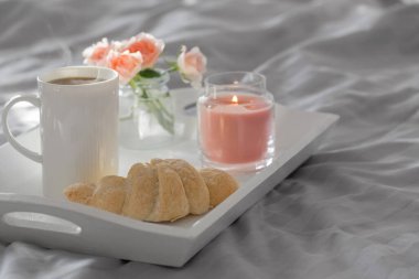 Yatak odasında kruvasan ve pembe güllerle bir fincan kahve.