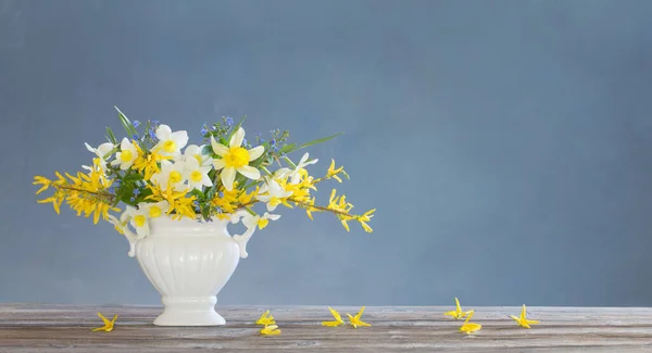 青い背景の木のテーブルの上の花瓶に白と黄色の春の花 — ストック写真