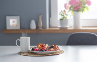 Ahududu ve yaban mersinli çörekler yuvarlak tabakta ve beyaz masada böğürtlenler