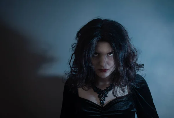 青い光の中の背景の壁に黒いドレスの若い怖い女性 — ストック写真