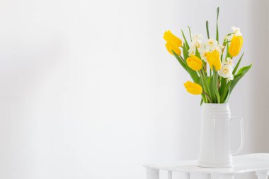 Beyaz arkaplanda vazoda beyaz ve sarı bahar çiçekleri