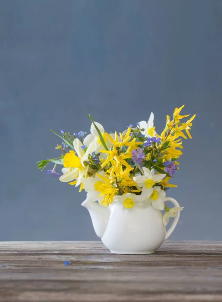 青の背景の木のテーブルの上に白と黄色の春の花 — ストック写真