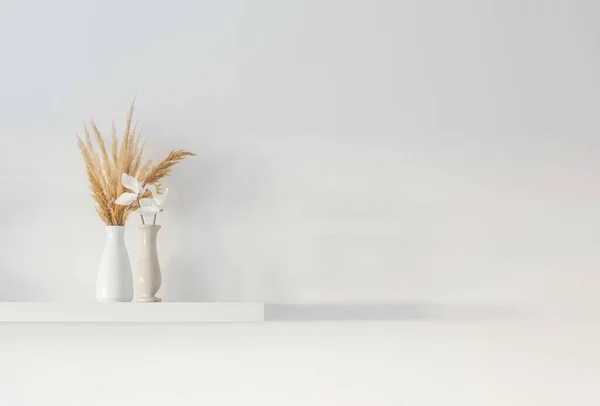 白墙上木制架子上的白色花瓶里有一束干野花 — 图库照片