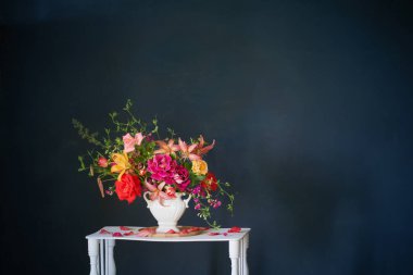 Vazoda bir buket yaz çiçeği. Koyu arkaplanda beyaz ahşap bir rafta.