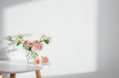 Pembe güller cam kavanozda beyaz masa üzerinde beyaz arka plan beyaz duvarda