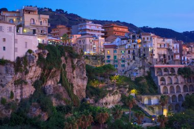 Dağ kayası üzerinde eski bir kasabanın akşam manzarası. Binalar ve sokak ışıkları alacakaranlık ışığı renginde.