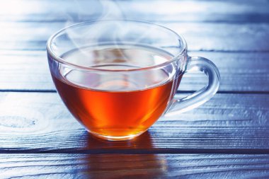 Mavi ışıklı soğuk arka planda, ahşap masanın üzerinde bir fincan kahverengi sıcak çay.